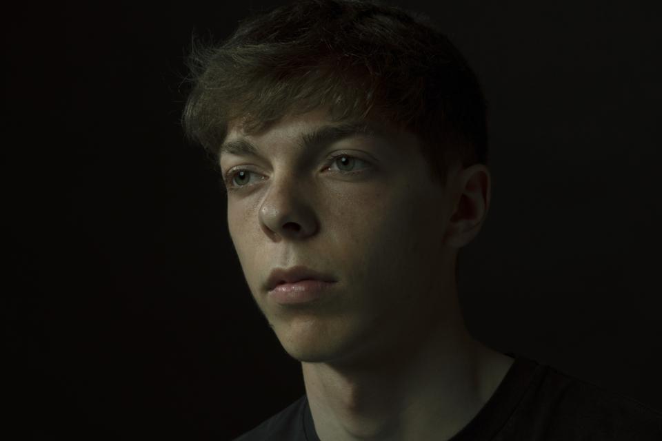 A young face emerges from darkness.
His gaze is steady, slightly unfocused.
Not confronting. Not withdrawing.
The black background absorbs everything unnecessary.
Only skin, breath, and silence remain.