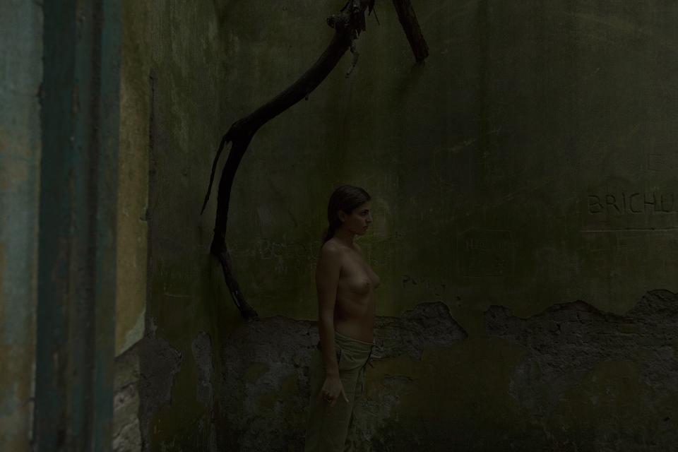 Green walls soaked in shadow.
Moisture stains the surface of time.
A woman stands still against the decay.
Light barely touches her skin.