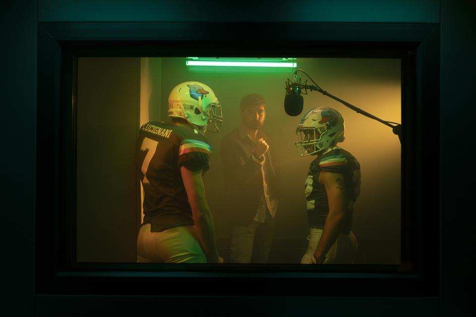 The booth is unchanged.
Same glass. Same microphone. Same walls.
But the air thickens with adrenaline.
Neon burns green like stadium lights before kickoff.
Breath heavier. Voices sharper. Strategy in motion.
HYPERCAST — one room, infinite arenas.
Tonight, sport.